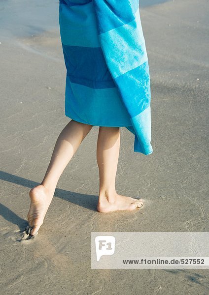 Kind in Handtuch gewickelt,  auf nassem Sand gehend