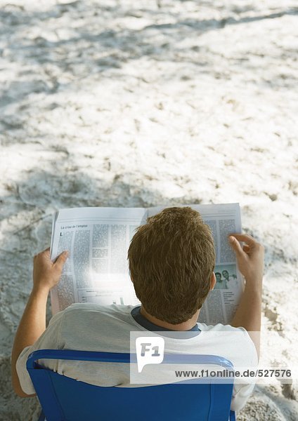 Mann sitzt im Strandkorb und liest Zeitung,  Rückansicht
