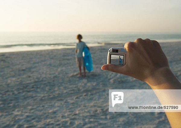 Fotografieren des Kindes mit Digitalkamera am Strand  Fokussierung auf Handkamera im Vordergrund