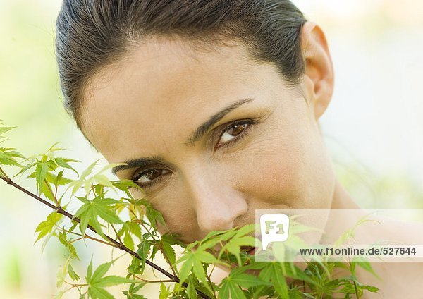 Frau versteckt Gesicht hinter Blättern