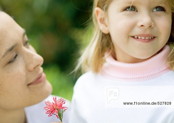 Mädchen mit Blume schaut auf  während Mutter sie ansieht.