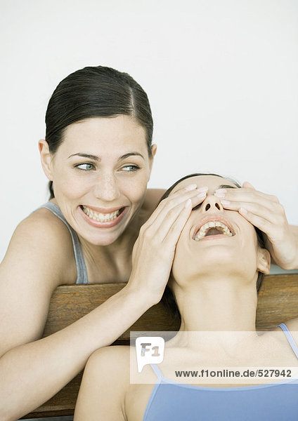 Young woman covering her friend's eyes  both smiling  portrait