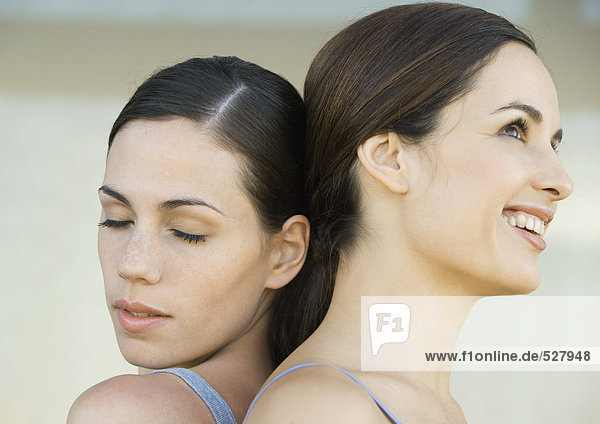 Two young women back to back  one with closed eyes while the other one is smiling  close-up