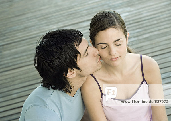 Young man kissing his girlfriend on the cheek  closed eyes  portrait