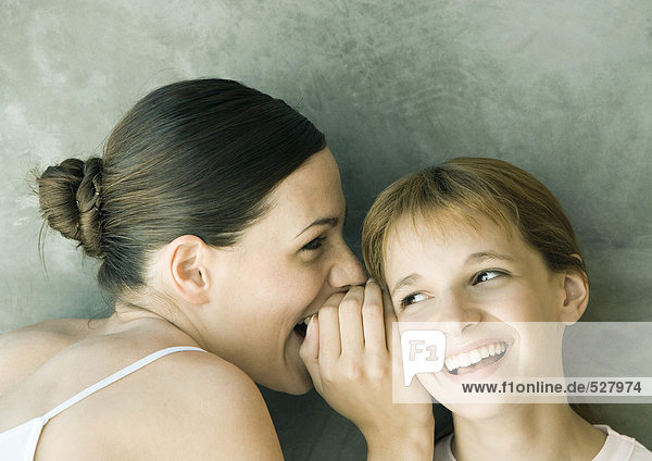 Young woman whispering to girl  both laughing  portrait  close-up
