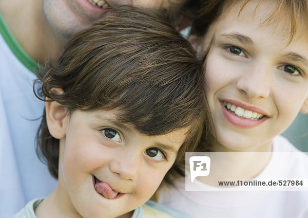 Vater mit zwei Kindern  Junge mit herausgestreckter Zunge  Mädchen und Vater lächelnd  Porträt  extreme Nahaufnahme