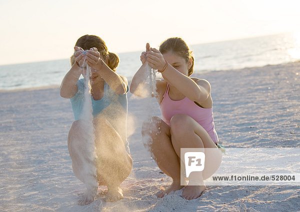 Zwei Mädchen  die Sand durch die Hände am Strand laufen lassen