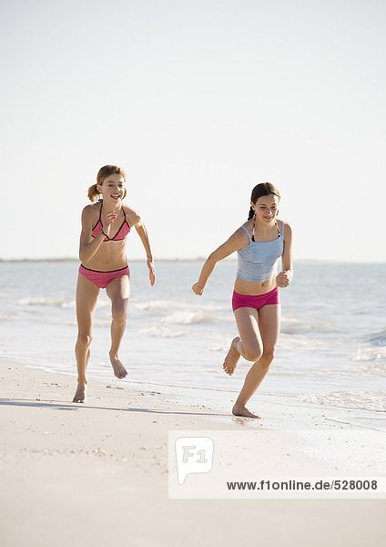 Two preteen girls running on beach