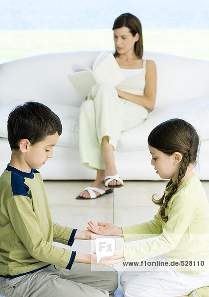 Junge und Mädchen spielen Spiel  während die Mutter im Hintergrund liest.