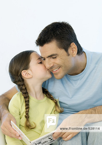 Girl kissing father's cheek while he holds book