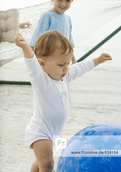 Baby reaching for ball on beach