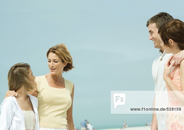 Mother and teenage daughter talking to couple on beach