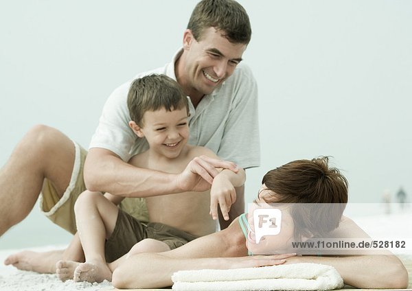 Family on beach  man and son bothering woman while she's lying down