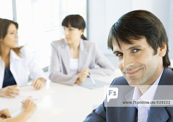 Businessman smiling  meeting in background  portrait