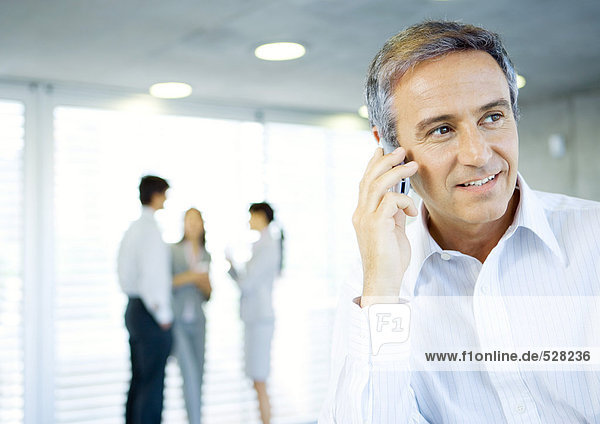 Mature businessman using cell phone  colleagues talking in background
