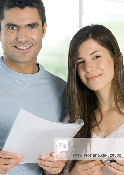 Paar haltend Dokument und Rechner  lächelnd auf Kamera