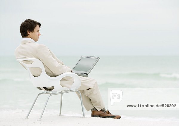 Geschäftsmann sitzend im Stuhl am Strand  mit Laptop