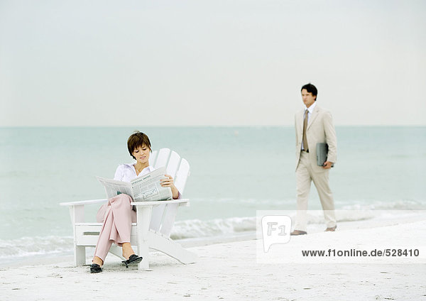 Frau sitzt am Strand und liest Zeitung als Geschäftsmann mit Laptop-Ansatz