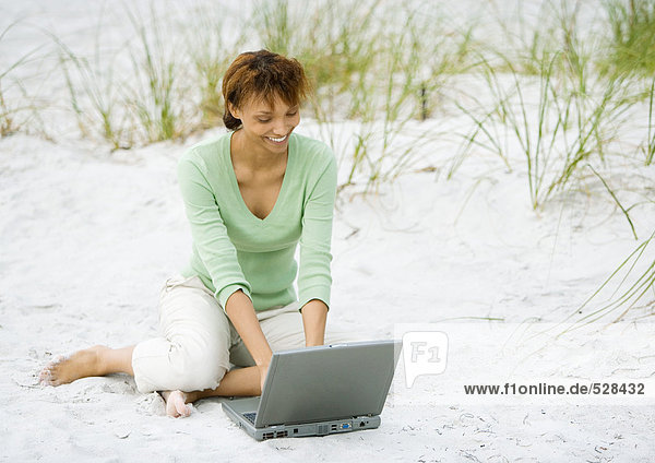 Frau auf Sand sitzend  mit Laptop