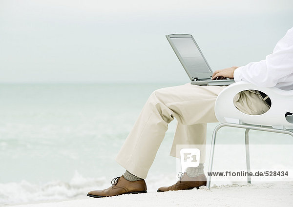 Geschäftsmann im Sessel sitzend  mit Laptop am Strand  Taille unten