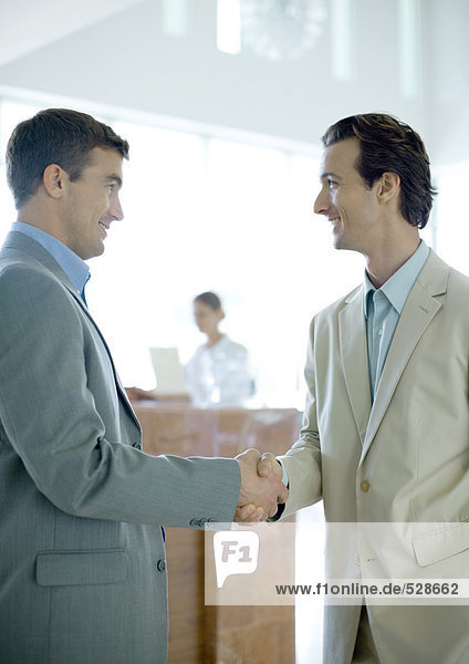 Two businessmen shaking hands in lobby