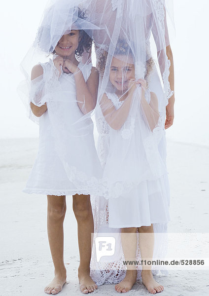 Blumenmädchen unter dem Brautschleier am Strand stehend