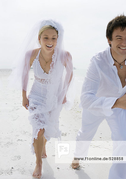 Braut und Bräutigam rennen am Strand
