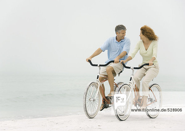 Mature couple riding bikes on beach