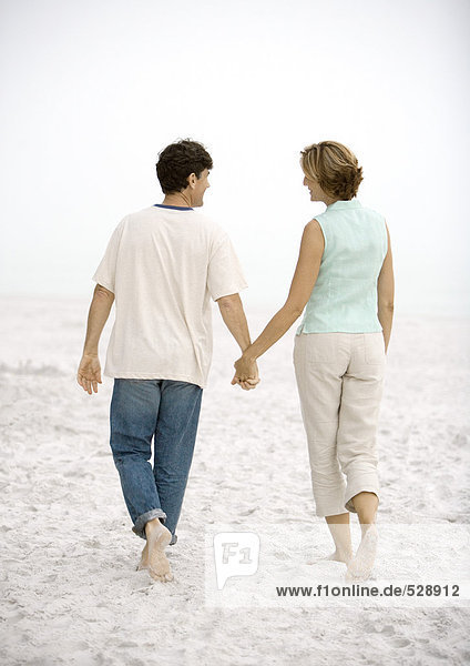 Mature couple walking on beach  holding hands  rear view