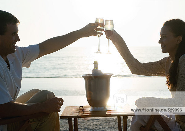 Young couple clinking champagne glasses on beach