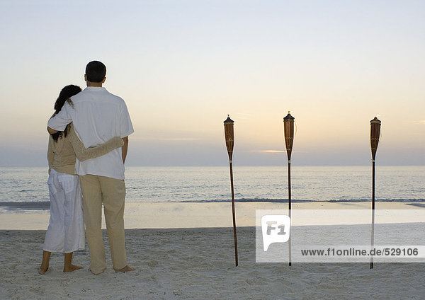 Paar steht am Strand und beobachtet den Sonnenuntergang