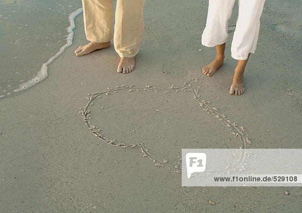 Couple standing by heart drawn in sand  view of knee down