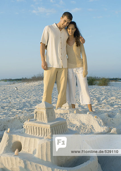 Couple standing on beach looking at sand castle