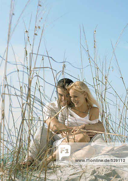 Couple sitting in dune grass  embracing