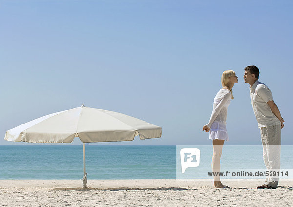 Couple standing on beach next to parasol  about to kiss