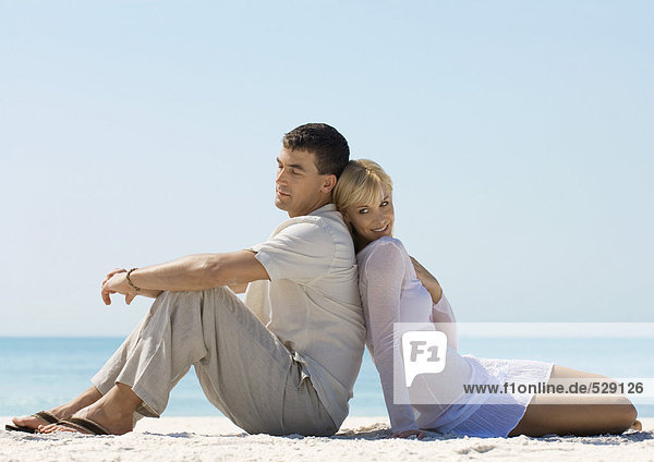 Couple sitting back to back on beach