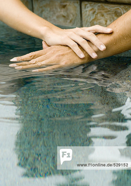 Frauen- und Männerhände auf der Oberfläche des Poolwassers gemeinsam