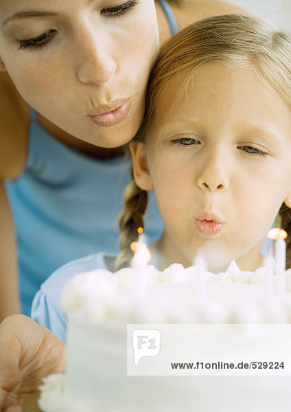 Mutter und Mädchen beim Ausblasen von Kerzen auf Geburtstagskuchen