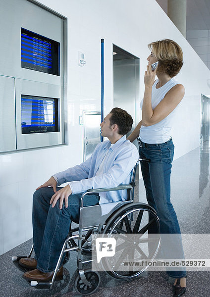 Frau und Mann im Rollstuhl beim Blick auf das Abflugbrett am Flughafen