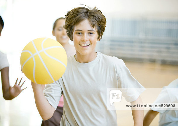 Teenager-Junge läuft mit Basketball in der Turnhalle  gefolgt von Klassenkameraden