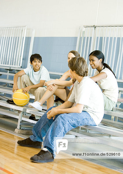 Gruppe von Jugendlichen sitzt mit Basketball auf Tribünen in der Schulsporthalle