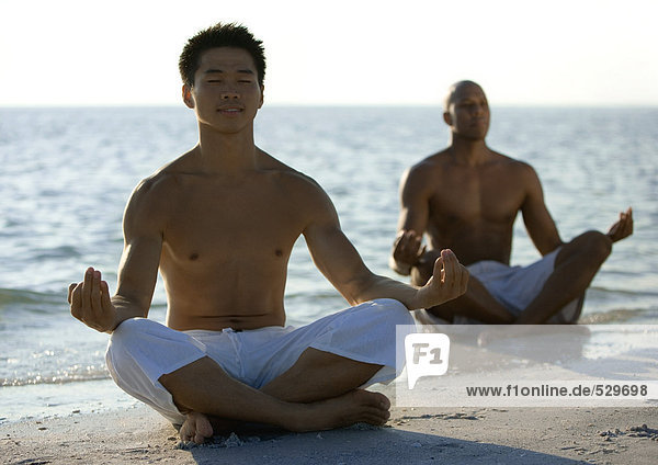 Zwei Männer meditieren am Strand