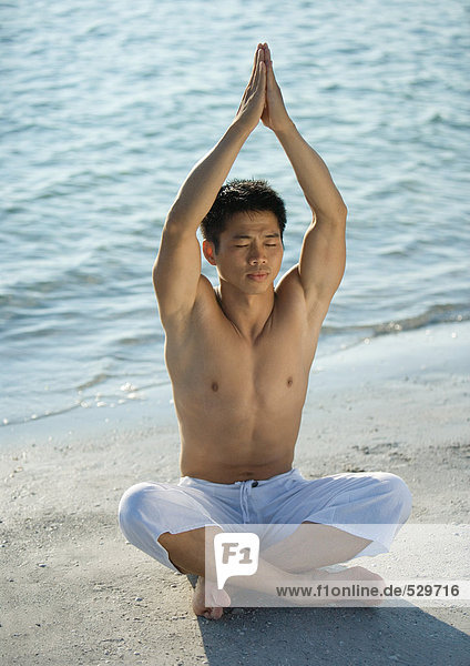 Mann am Strand sitzend in Yogaposition