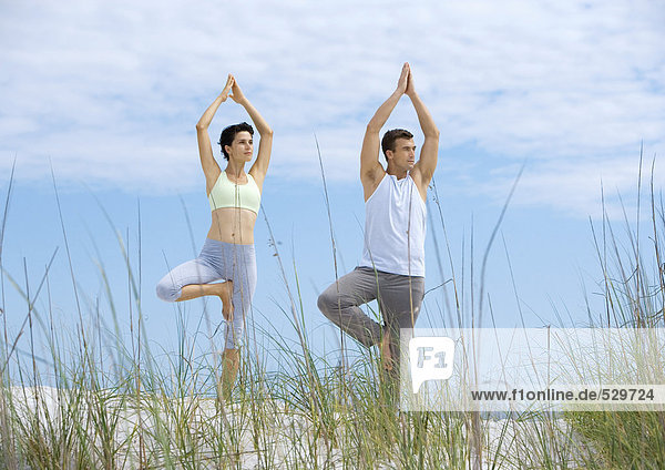 Paar stehend in Yogabaum-Pose am Strand