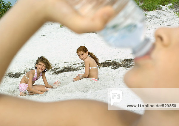 Kinder spielen am Strand  Junge trinkt Wasser im Vordergrund
