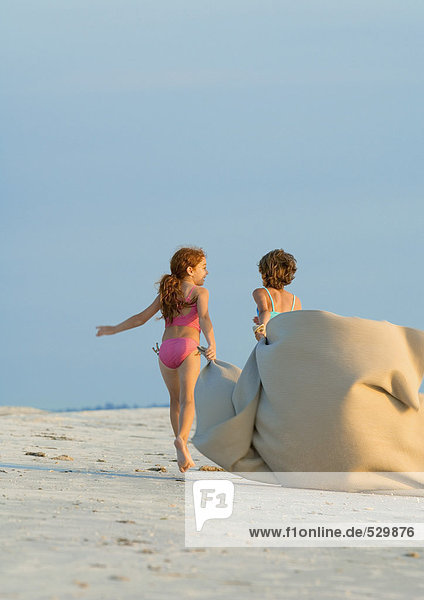 Zwei Mädchen mit Decke im Wind am Strand
