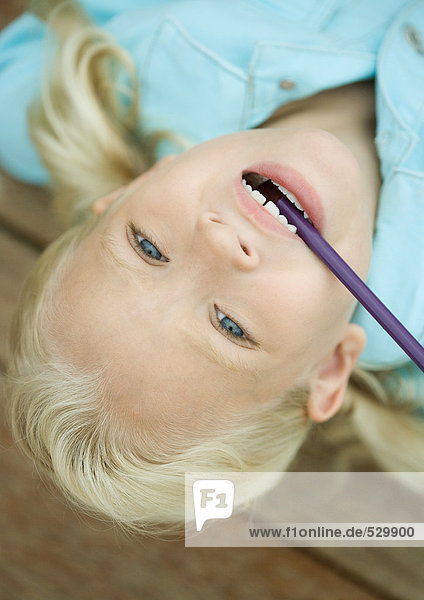 Little girl with head upside down and pencil in mouth