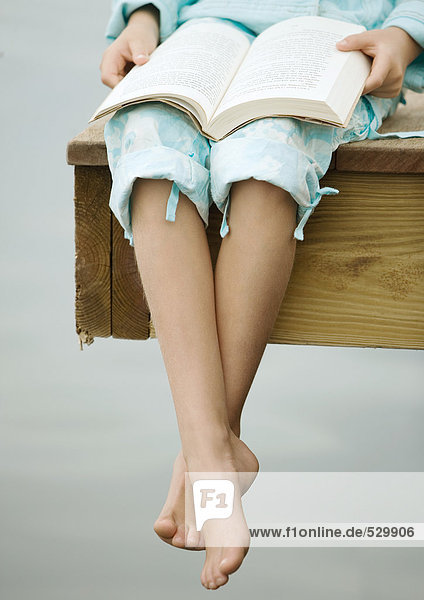 Girl sitting on edge of dock  reading book