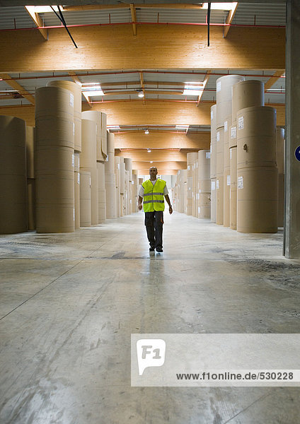 Man walking through rolls of paper in warehouse