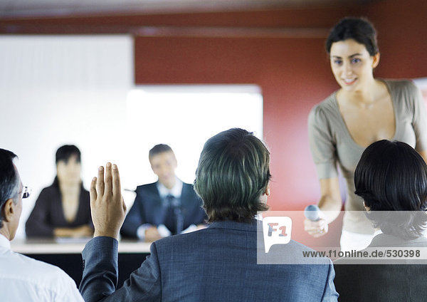 Executives sitting in seminar  woman holding microphone to man raising hand